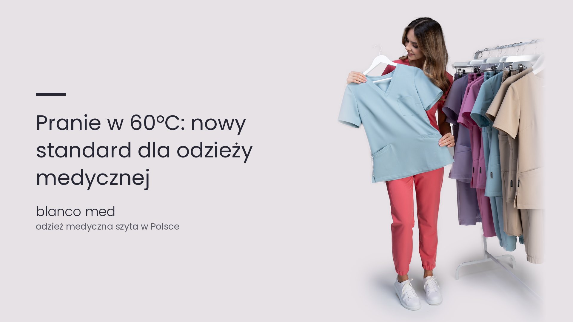 Kobieta w koralowym komplecie trzyma błękitną bluzę medyczną przy wieszaku. Pranie w 60°C, nowy obowiązkowy standard w szpitalach dla odzieży medycznej z elastanem
